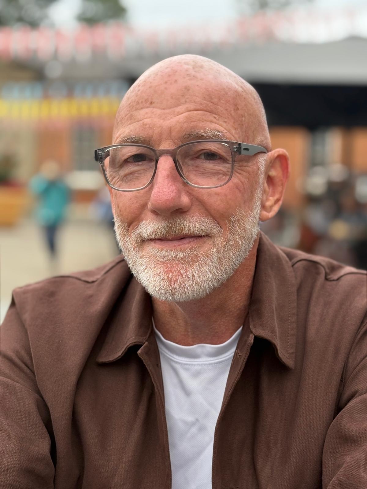 Adam Cairns, smiling, in a brown overshirt and glasses