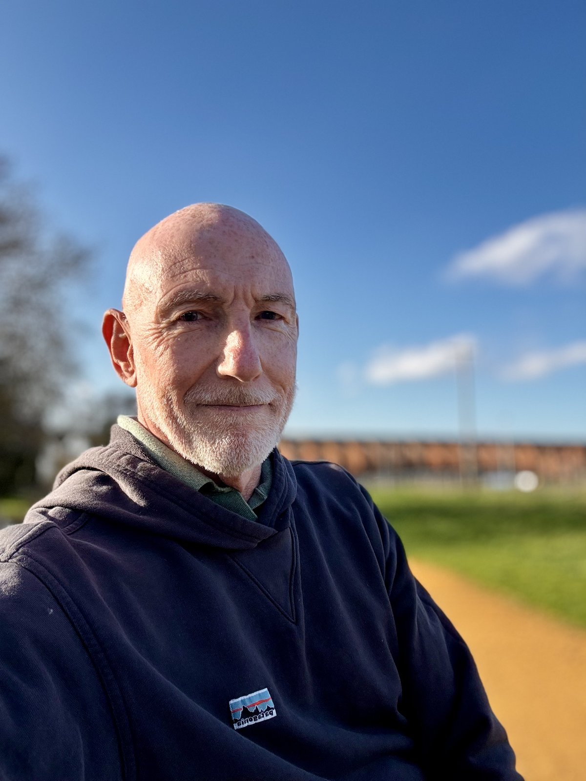 Adam Cairns, smiling, in a navy hoodie outdoors under a blue sky